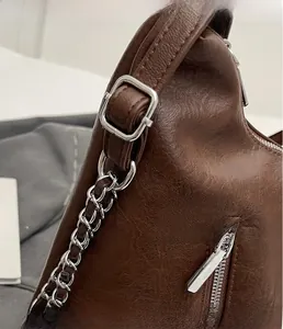 Detail view of brown textured leather backpack with silver chain strap and metal buckle