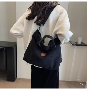 Detail showing a black corduroy tote bag with brown leather logo and adjustable strap