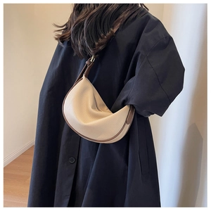 Détail d'un sac demi-lune en cuir grainé beige avec bordure marron et surpiqûres