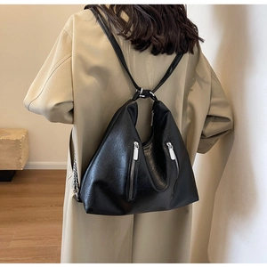 Rear view of model wearing a black soft PU leather backpack with silver chain zippers