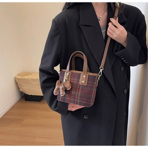 Détail du sac seau à carreaux avec poignées en cuir marron et breloque chien ballon
