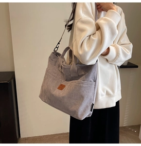 Detail of gray corduroy tote bag featuring a leather logo patch and adjustable strap