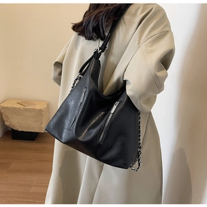 Detail of black soft PU leather tote bag with silver chain strap on model in a minimalist room
