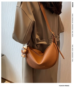 Detail of tan pebble leather hobo bag with monkey charm worn with a stylish trench coat