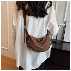 Gros plan du sac bandoulière en cuir marron avec motif litchi sur modèle avec texture