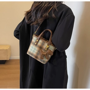 Détail du sac seau vintage en laine à carreaux avec garniture en cuir et charm chiot