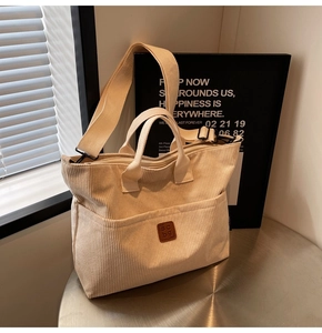 Close-up of cream corduroy tote bag featuring brown leather logo and metal hardware