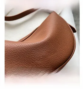 Detail of brown lychee leather saddle bag with gold logo lettering and fine stitching