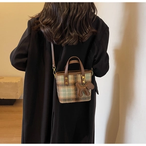Détail du sac seau à carreaux en laine avec poignées en cuir marron et bijou de sac