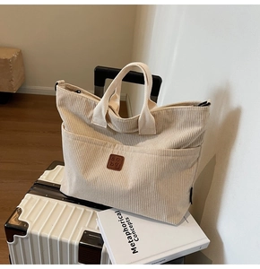 Detailed close-up of beige corduroy tote bag texture and brown leather label on luggage