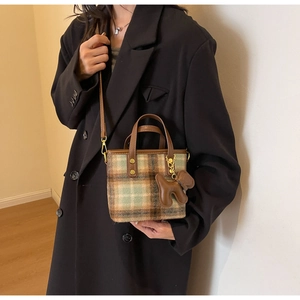 Détail du sac seau en laine à carreaux avec poignées en cuir marron et pendentif ours