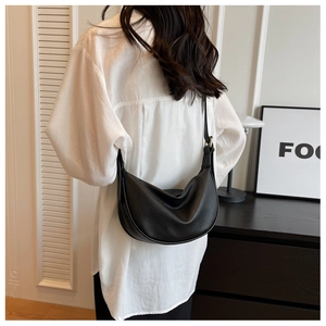 Gros plan d'un sac hobo noir en cuir grainé sur un modèle en tenue blanche minimaliste