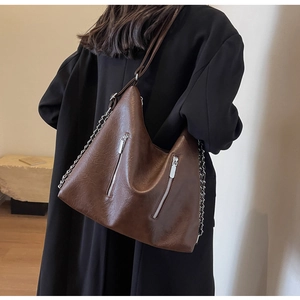 Detail of dark brown leather crossbody bag with silver chains worn over a black coat