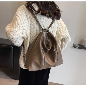 Detail of vintage brown leather backpack showing metal chain straps and vertical zippers