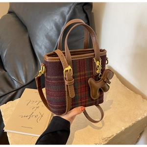 Détail du sac seau en laine à carreaux avec anses en cuir et un charme ours brun