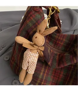 Detail showing a knitted rabbit charm with brown ribbon on a textured checkered bag