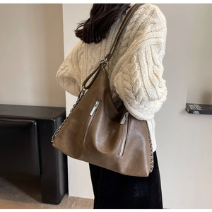 Detail of a large brown hobo bag featuring silver zippers and chain strap on a model