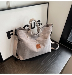 Detail of light gray corduroy tote bag showing fine texture and brown leather logo tag