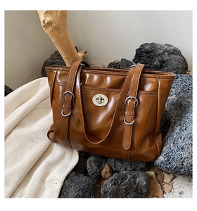 Detail of brown faux leather tote with silver twist-lock closure on textured background