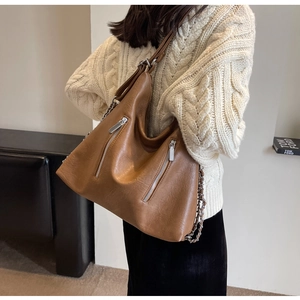 Detail of a brown leather tote bag featuring dual vertical zippers and chain strap