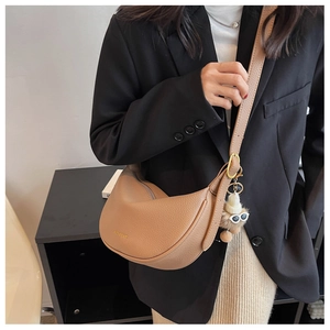 Detail of khaki half-moon crossbody bag with litchi texture and plush charm on model