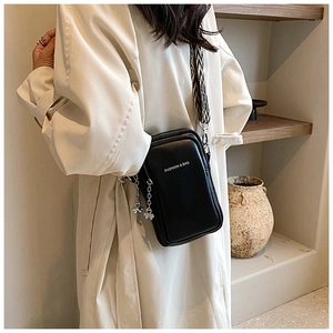 Détail du sac de téléphone noir en cuir avec bandoulière tissée et charms trèfle en décor