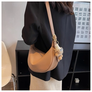 Detail of khaki crescent saddle bag in litchi grain leather with cute monster plush charm