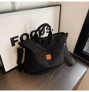 Close-up of black corduroy tote bag with leather scbg logo and wide shoulder strap