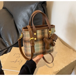 Détail du sac seau en tweed à carreaux avec poignée en cuir brun et pendentif chien