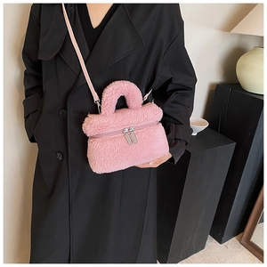 Detail van roze pluche crossbodytas met verstelbare riem en zilveren rits op een zwarte jas