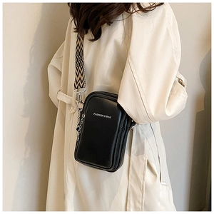 Détail d'un sac à bandoulière noir avec large sangle géométrique et chaîne métallique