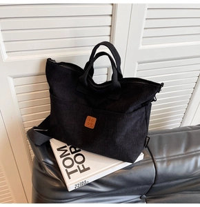 Detail of black corduroy tote bag showing striped texture and leather logo patch