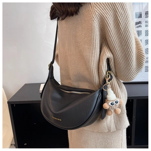 Detail of black pebbled hobo bag with gold logo and cute plush dog charm on shoulder