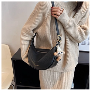 Close-up of black lychee leather crescent bag with a cute monkey keychain detail