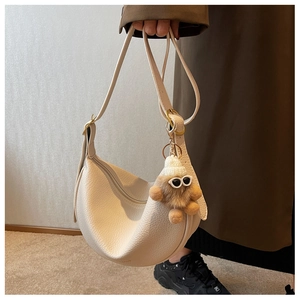 Close-up of creamy white lychee leather saddle bag with a cute bear plush pendant charm
