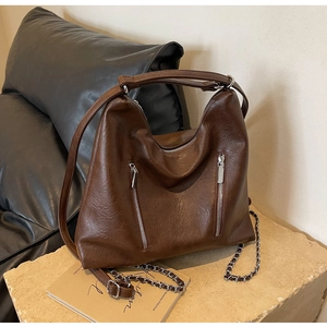 Detail of dark brown faux leather hobo bag with dual vertical zippers on stone surface