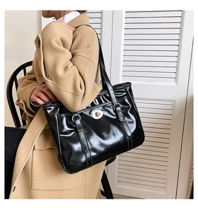 Detailed view of large black glossy tote bag with metal twist lock and slim straps