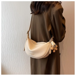 Detail of beige crescent leather bag with fashion text and cute bear charm on coat