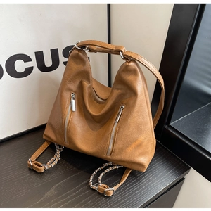 Close-up of caramel brown pebble leather bag featuring chain straps and dual front zippers