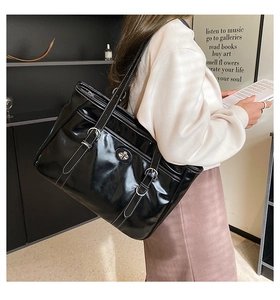 Macro view of black patent leather tote bag with white contrast stitching and metal buckle