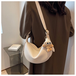 Detail of white lychee leather saddle bag with plush monster charm on fashion model