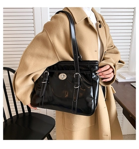 Detail of black patent leather tote bag with silver buckle on model in tan coat