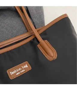 Close-up of stitching detail on black nylon tote bag with brown leather handle connector