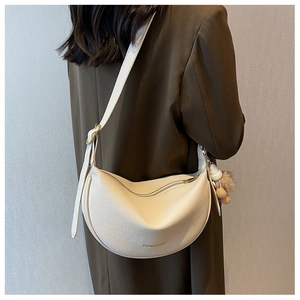 Close-up of beige lychee leather half-moon bag with shoulder strap and pompom charm