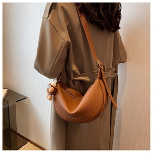 Detail of brown litchi leather saddle bag with wide strap and plush bear charm