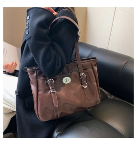 Detail of deep brown leather tote bag featuring a silver twist lock and slim shoulder straps