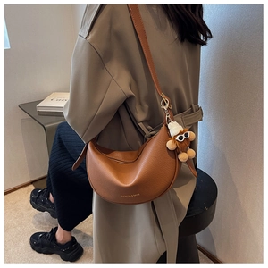 Brown lychee leather crescent bag with plush charm shown in a minimalist interior setting
