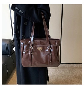 Detail of dark brown glossy leather tote bag with silver twist lock and white stitching