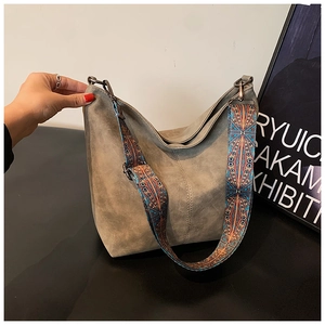 Detail of grey suede shoulder bag featuring a bohemian colorful woven wide strap