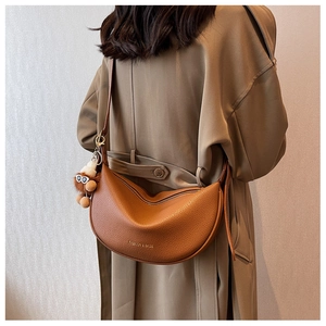 Brown litchi grain leather half-moon crossbody bag shown on a trench coat model